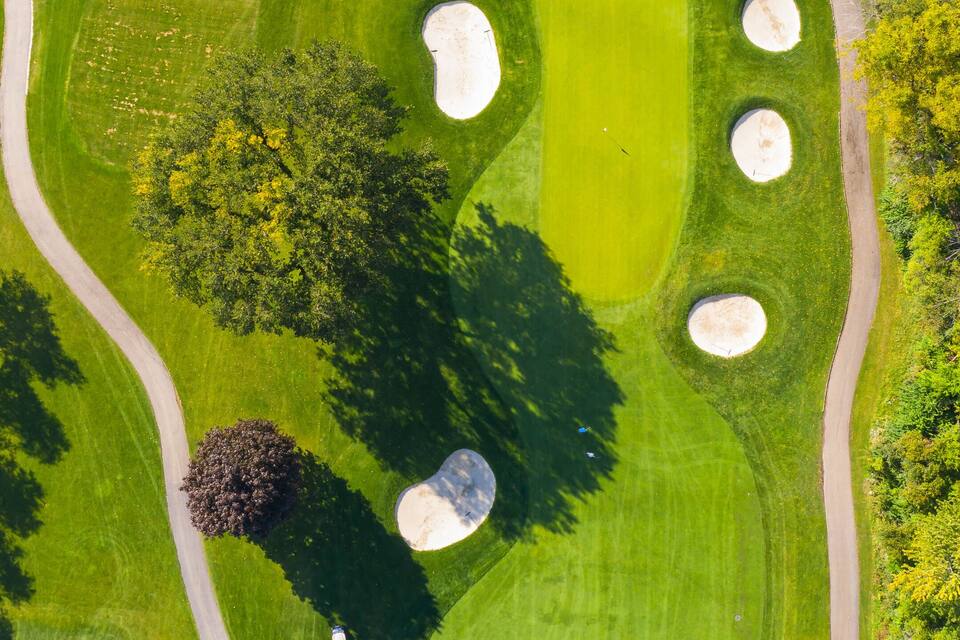Um campo de golfe com bunkers de areia, um lago e um caminho sinuoso.