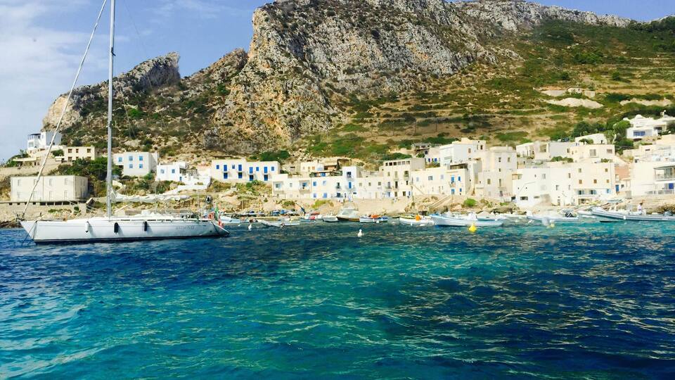 A coastal village with white buildings, a rocky hill, and boats in the water.
