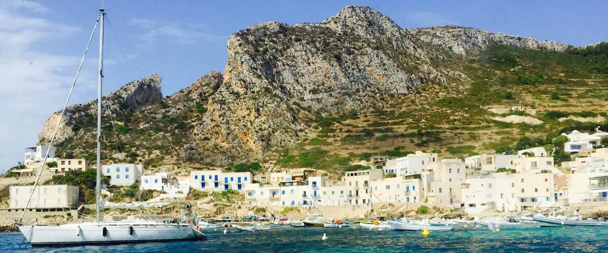 A coastal village with white buildings, a rocky hill, and boats in the water.