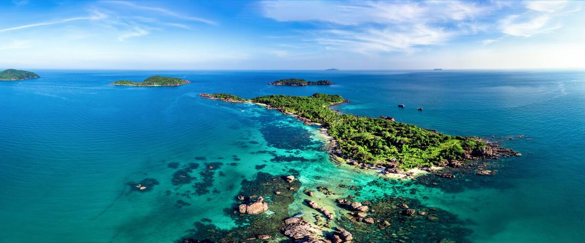 A coastal landscape with clear turquoise waters, a sandy beach, and lush green islands.