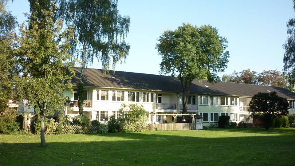 A two-story house with a balcony, surrounded by a well-maintained lawn and trees.