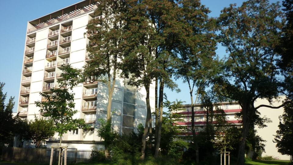 A multi-story residential building with balconies, surrounded by trees and a grassy area.