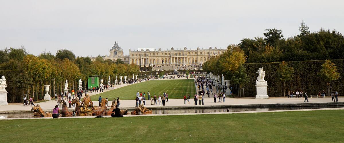 A large, historic building with a grand facade, a well-maintained lawn, and a statue in the foreground.