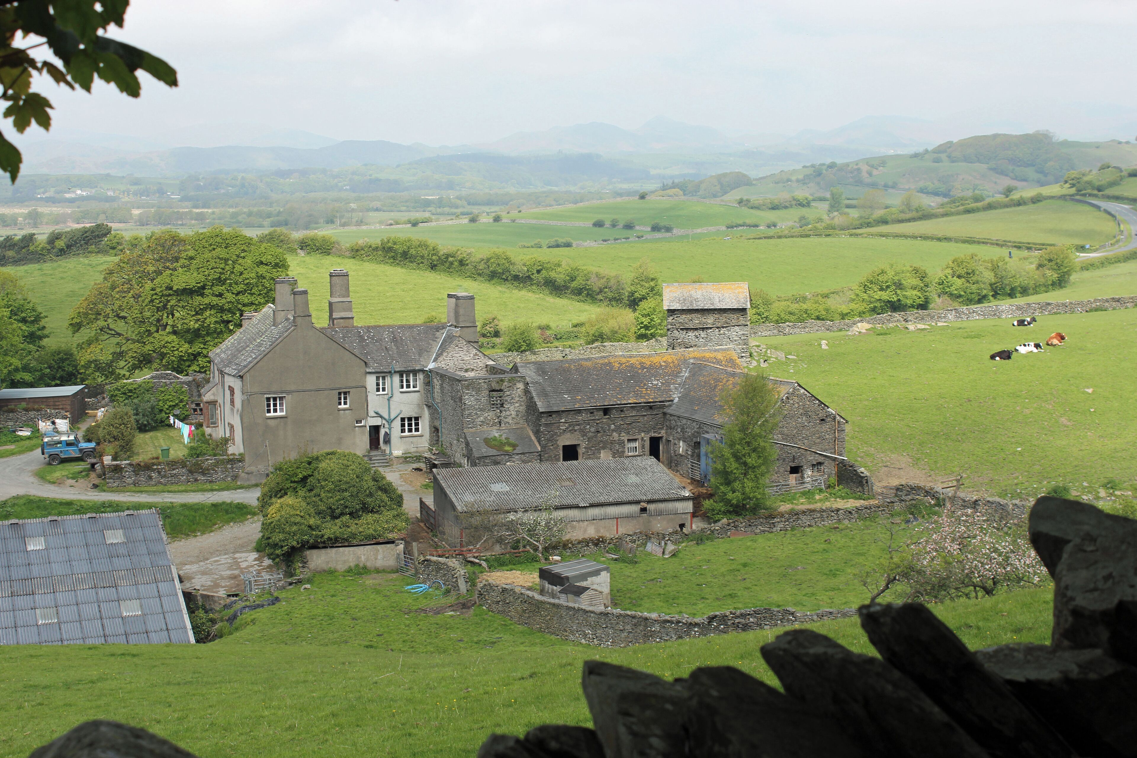 A rural landscape with a stone house, green fields, and distant mountains.