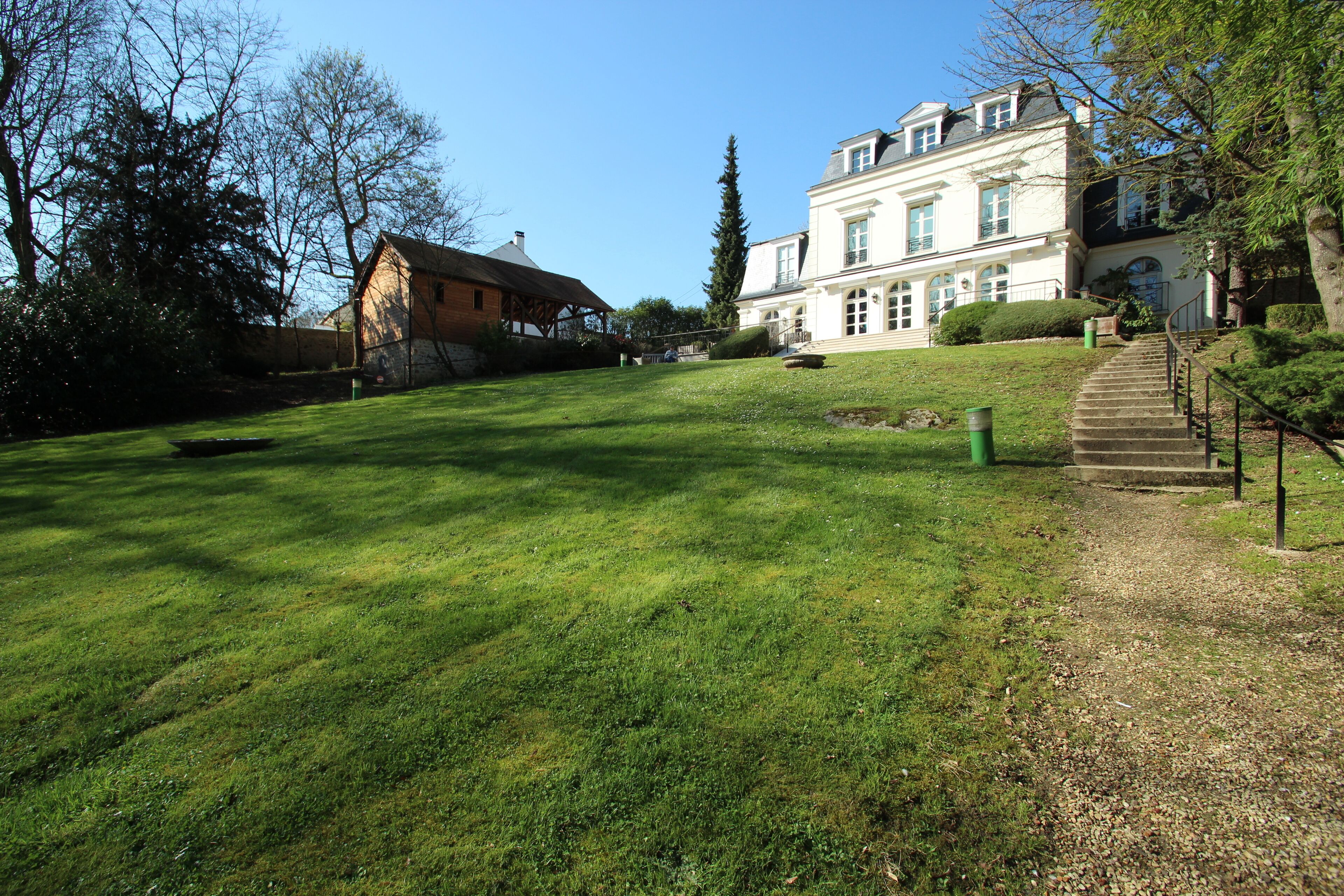 A large, white mansion with a well-maintained lawn and a gravel path leading to the entrance.