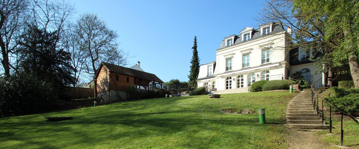 A large, white mansion with a well-maintained lawn and a gravel path leading to the entrance.
