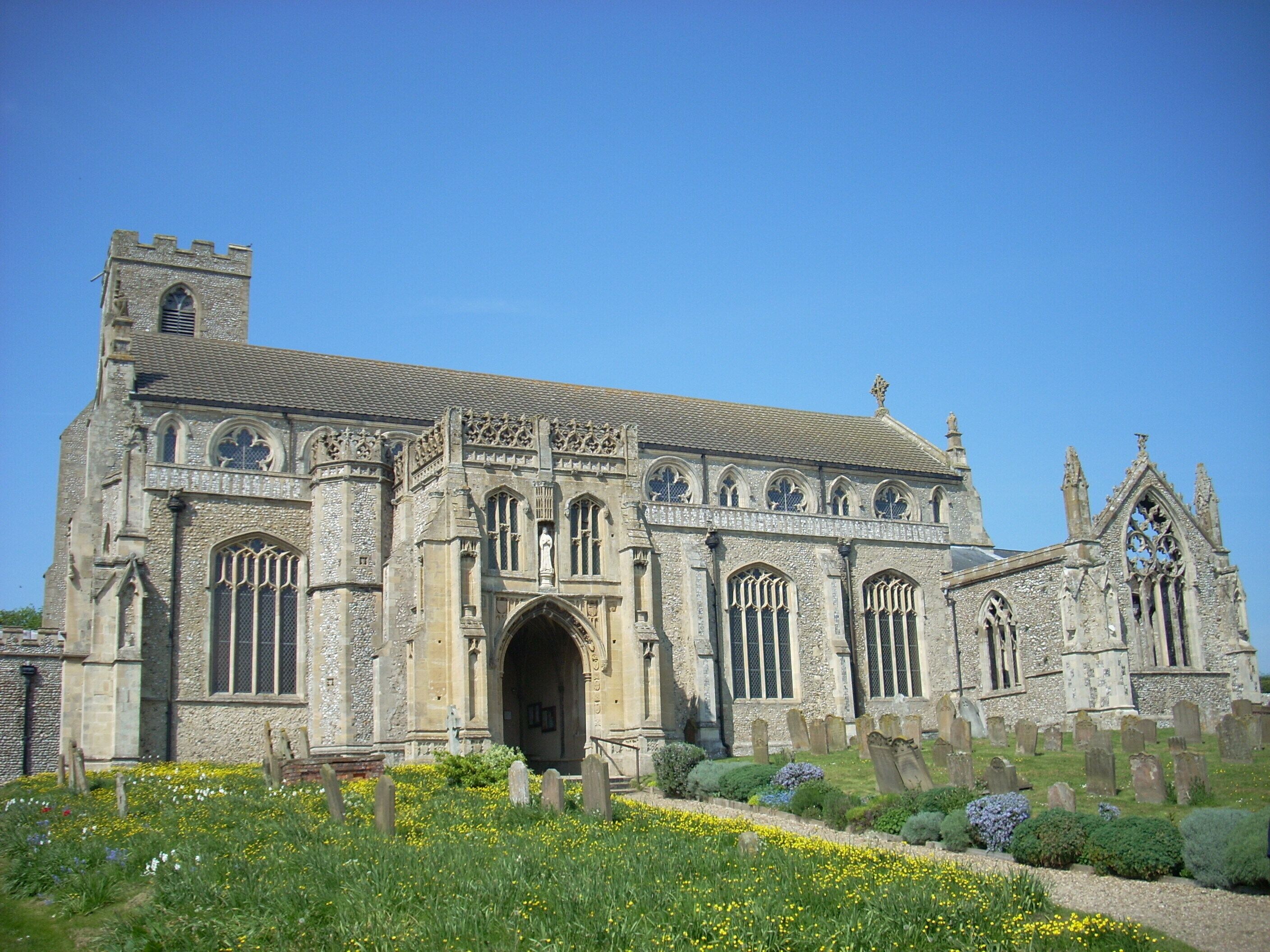 A historic church with a prominent tower, arched windows, and a well-maintained garden with yellow flowers.