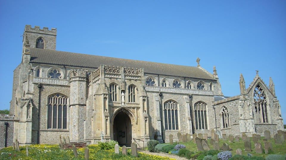A historic church with a prominent tower, arched windows, and a well-maintained garden with yellow flowers.