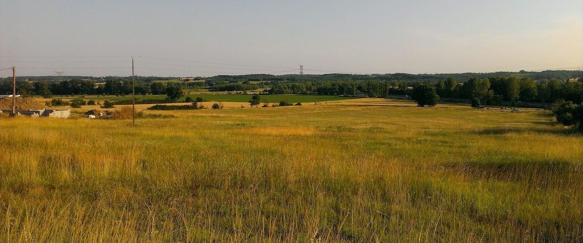 A rural landscape with a field, trees, and distant hills.