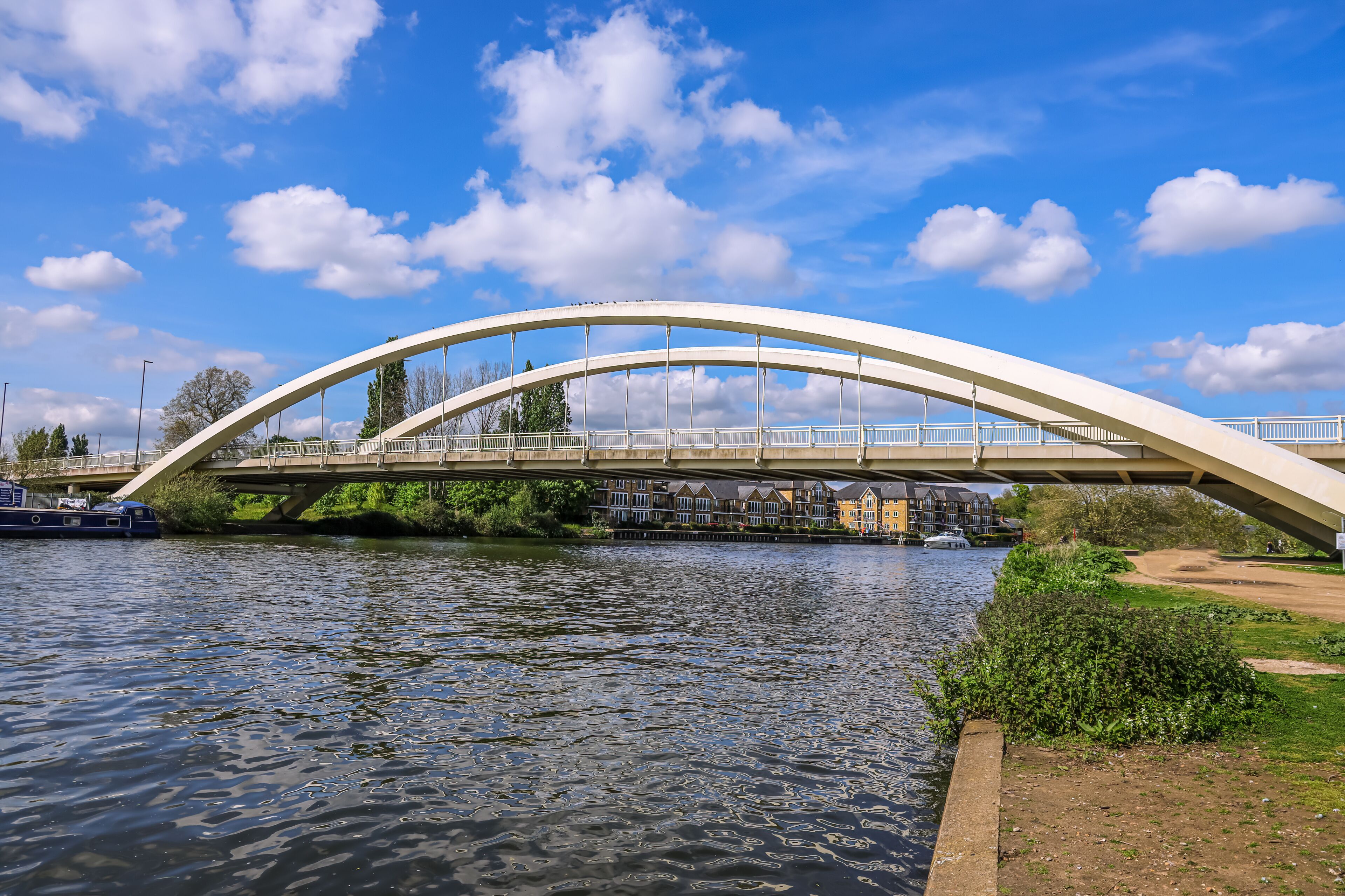 A white arched bridge over a river with houses in the background.