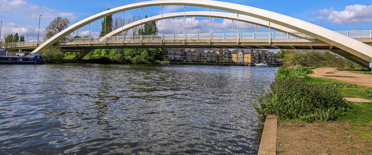 A white arched bridge over a river with houses in the background.