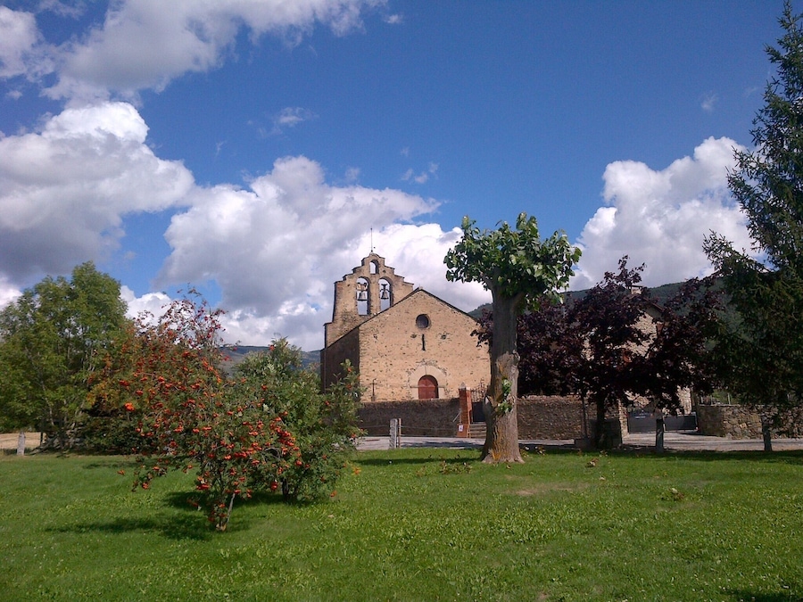 Una església amb un campanar, envoltada d'herba verda i arbres.
