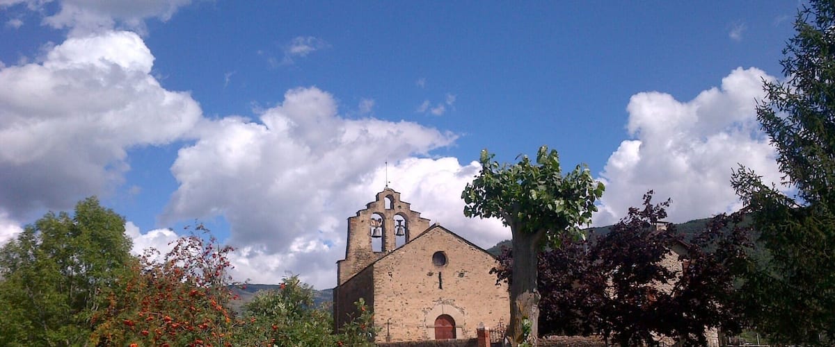 A church with a bell tower, surrounded by green grass and trees.
