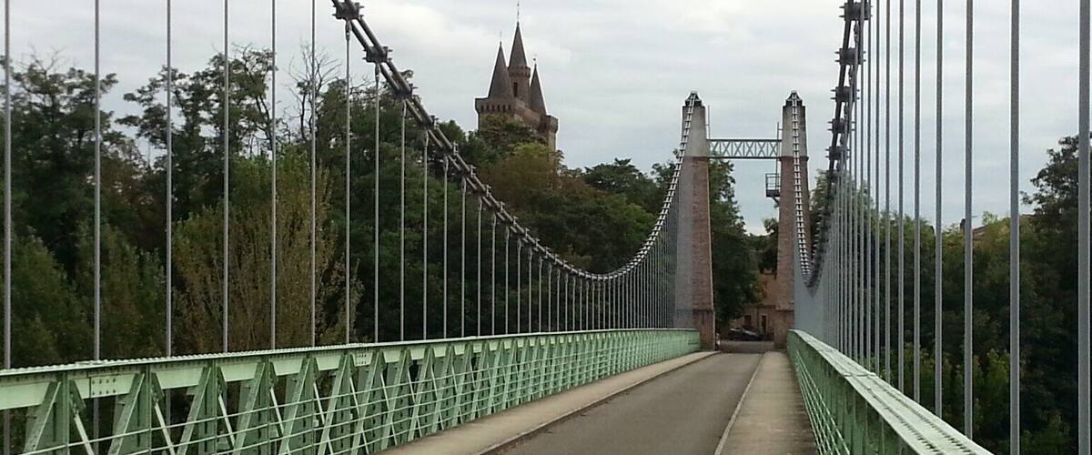 A green suspension bridge with a castle in the background.
