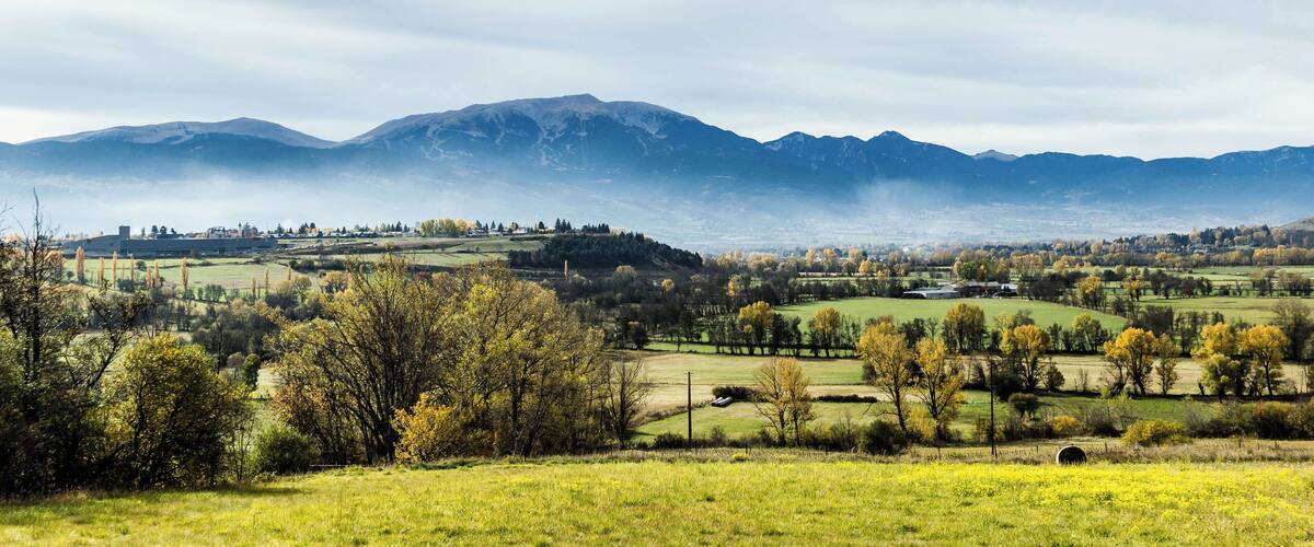 A mountainous landscape with rolling hills, scattered trees, and a clear sky.