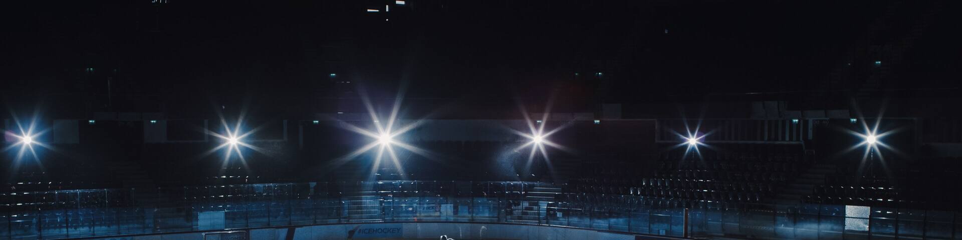 Ice Hockey Rink Arena: Professional Player Training Alone. Skates, Dribbles with Stick, Shooting, Hitting the Puck. Determined Athlete with Desire to Win, Be Champion. Cinematic Lights