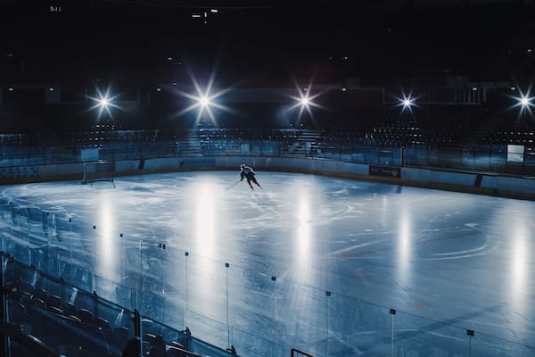 Ice Hockey Rink Arena: Professional Player Training Alone. Skates, Dribbles with Stick, Shooting, Hitting the Puck. Determined Athlete with Desire to Win, Be Champion. Cinematic Lights