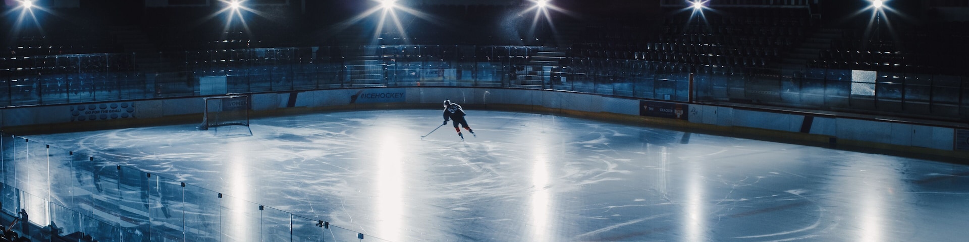 Ice Hockey Rink Arena: Professional Player Training Alone. Skates, Dribbles with Stick, Shooting, Hitting the Puck. Determined Athlete with Desire to Win, Be Champion. Cinematic Lights