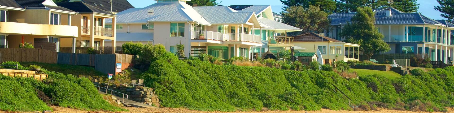 A beach with houses in the background and people walking along the shore.