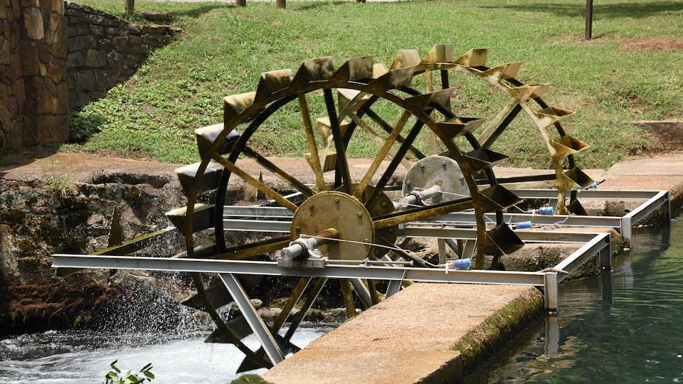 A large water wheel with a metal structure and a stone wall.