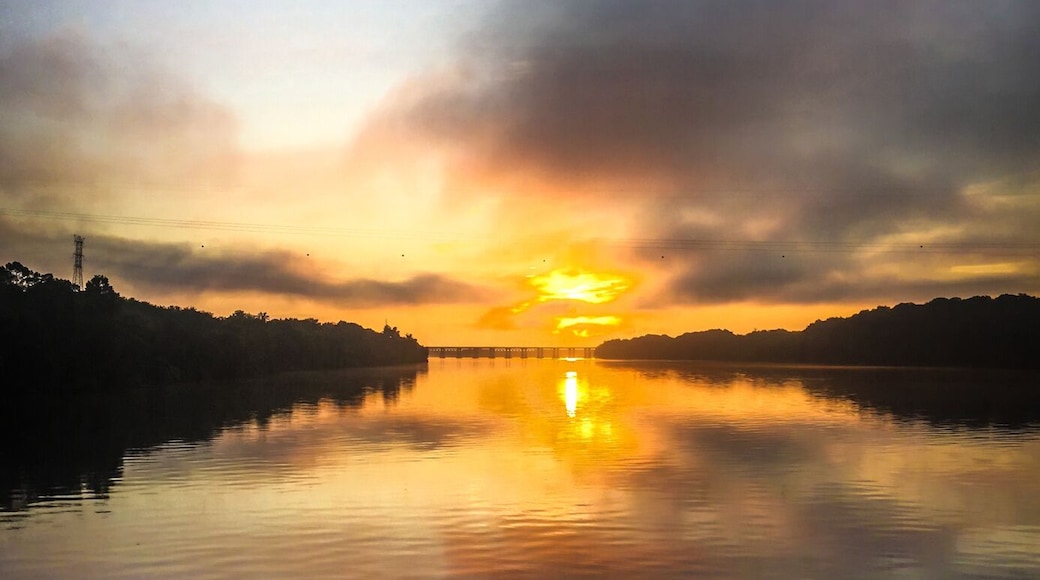 A calm river reflecting the sunset with a silhouette of trees and a distant power line structure.