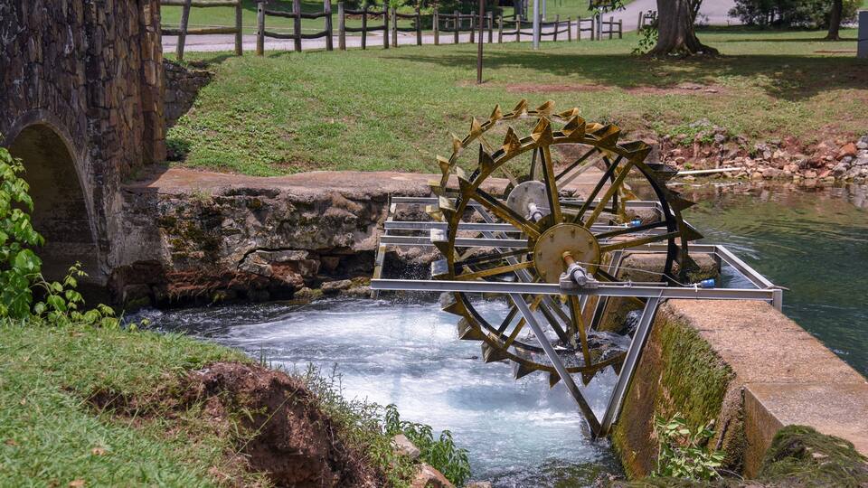 A water wheel near a stone bridge over a flowing stream.