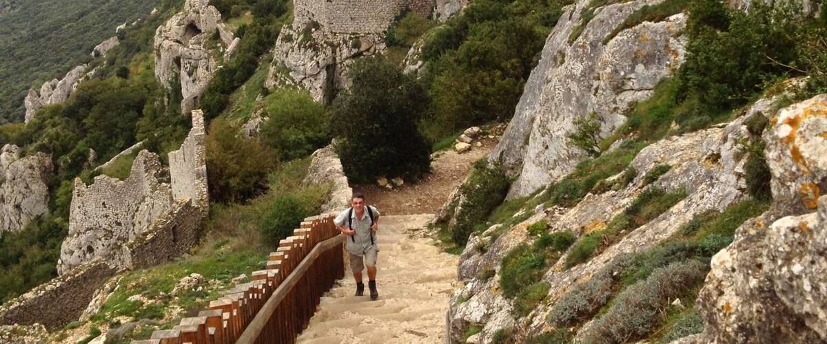 A stone pathway leading to a historic fortress on a mountain, surrounded by rocky terrain and greenery.