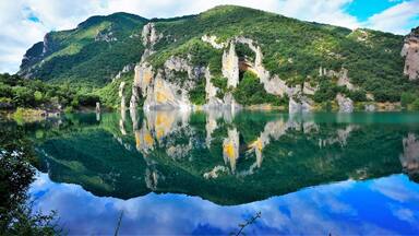 A clear lake reflecting cliffs and greenery.