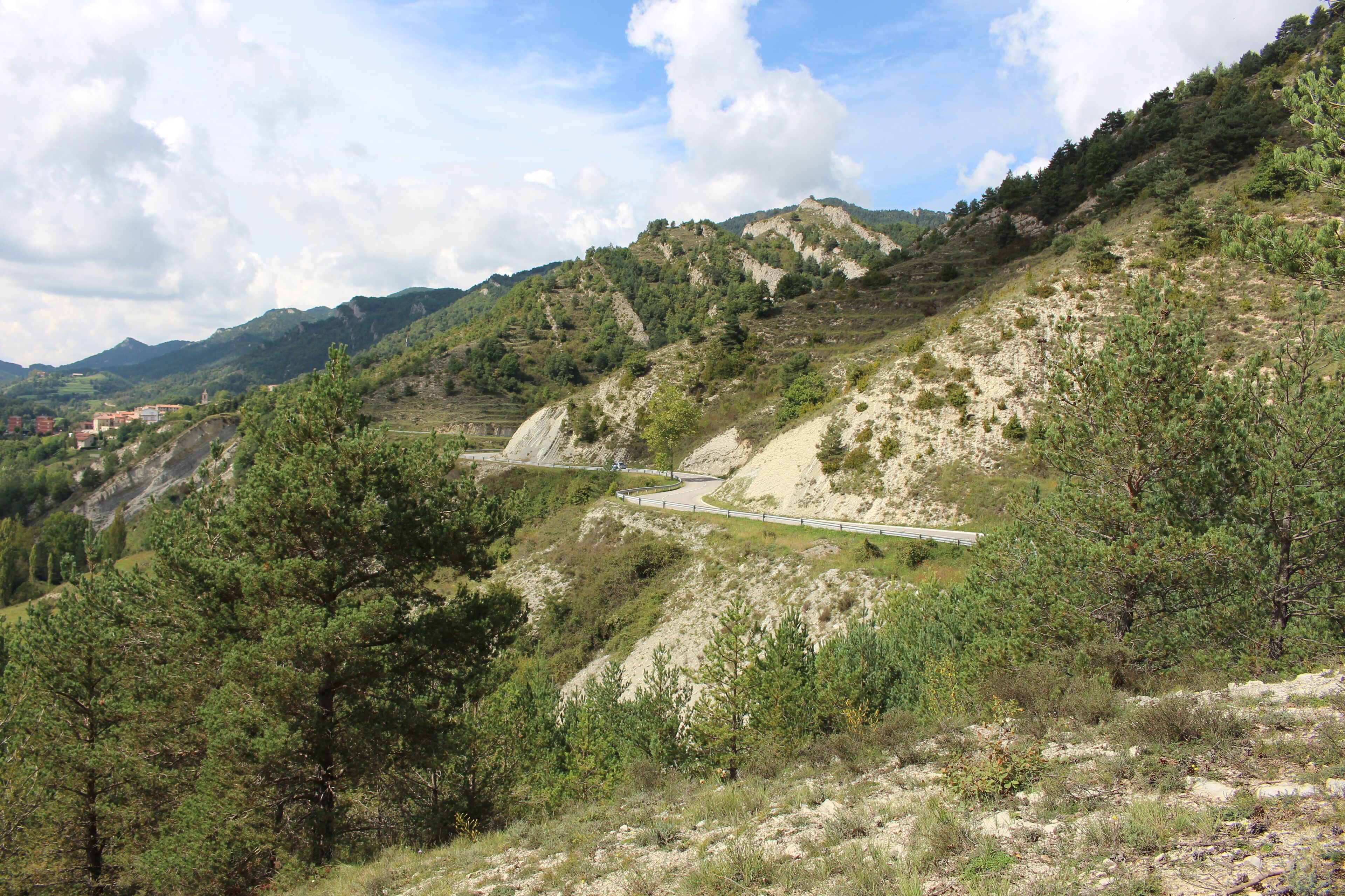 A winding road through a mountainous landscape with dense green forests and rocky terrain.