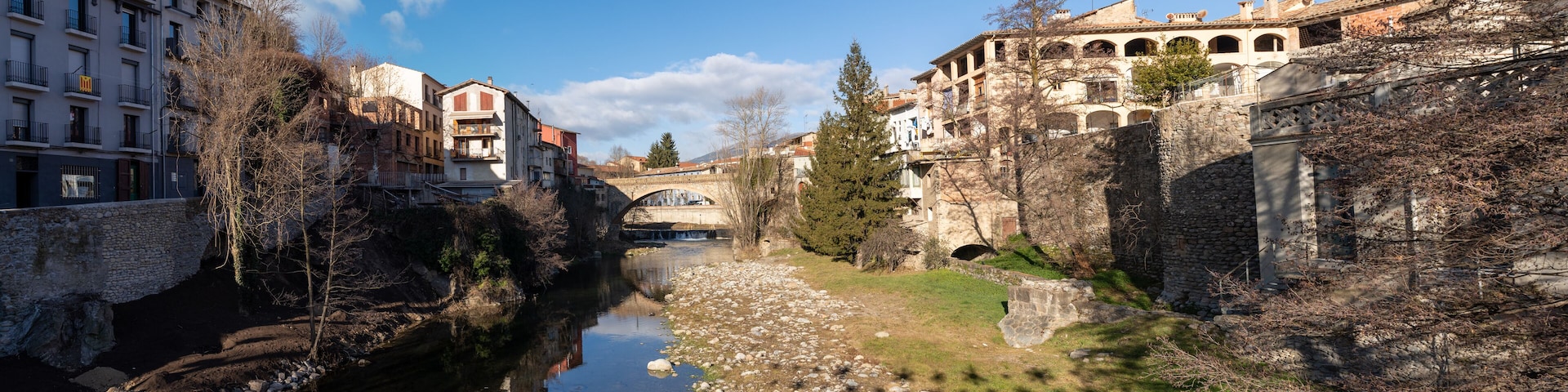 A river with buildings on both sides, a stone bridge, and trees.