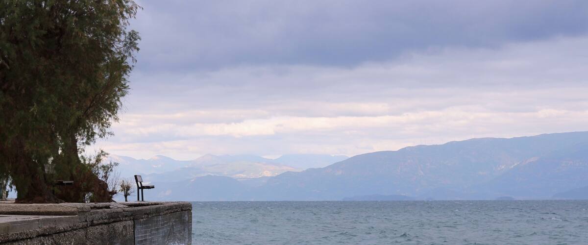 Bench at a dock at stormy weather and big waves at sea clouds and mountains at the background
