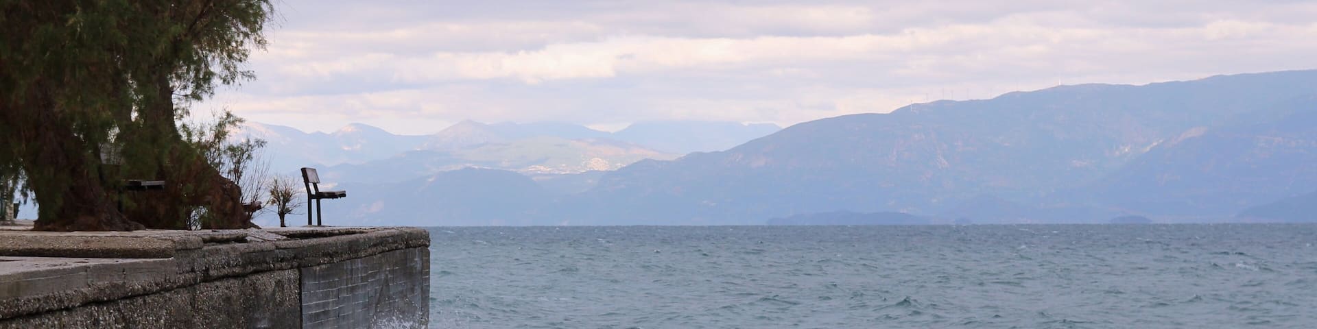 Bench at a dock at stormy weather and big waves at sea clouds and mountains at the background