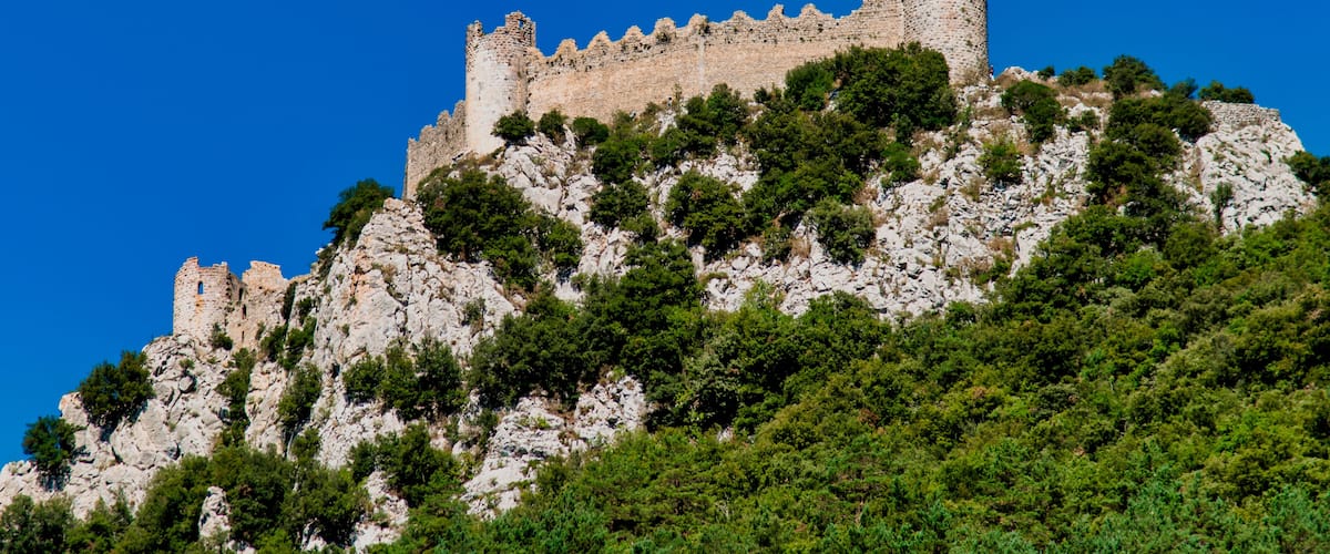 A historic stone castle atop a rocky hill with dense green foliage.