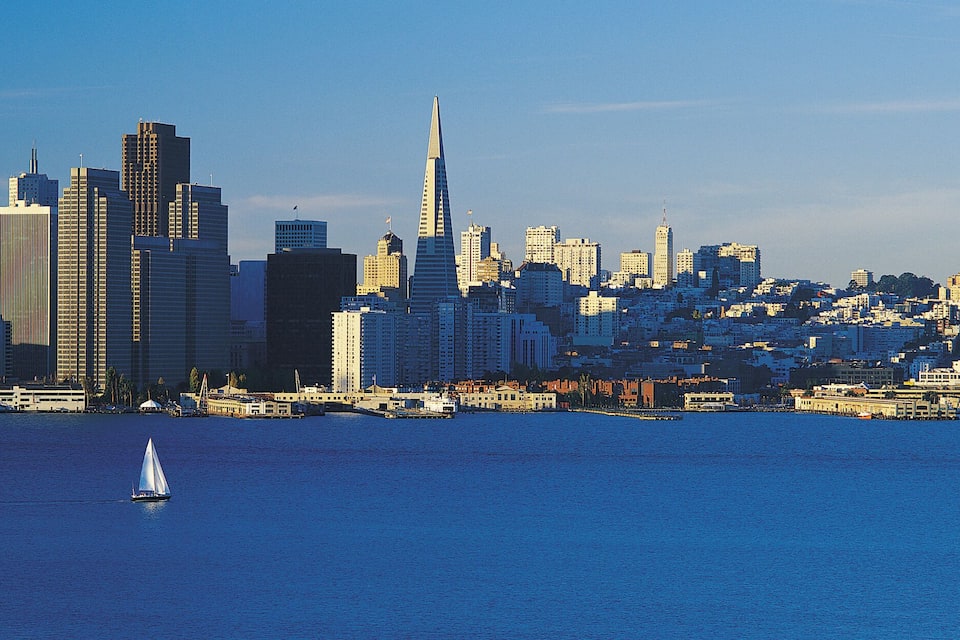 A city skyline with a prominent skyscraper, a body of water, and a sailboat.