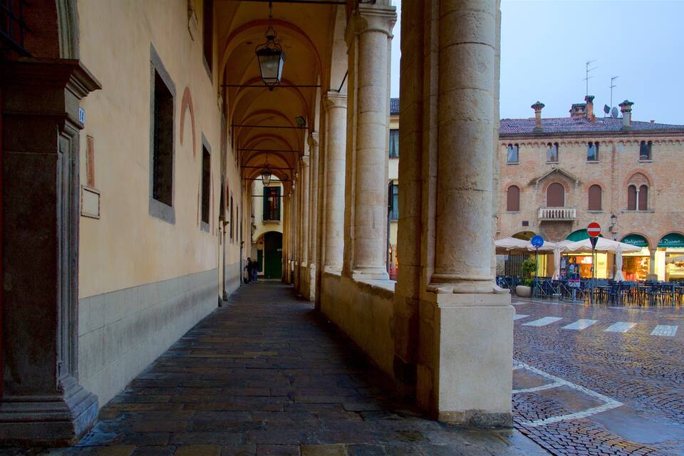 A cobblestone alleyway with arches and columns, leading to a building with outdoor seating.