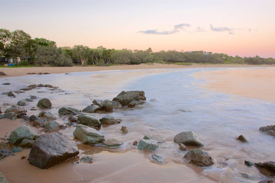 A beach with large rocks in the foreground and a calm sea.