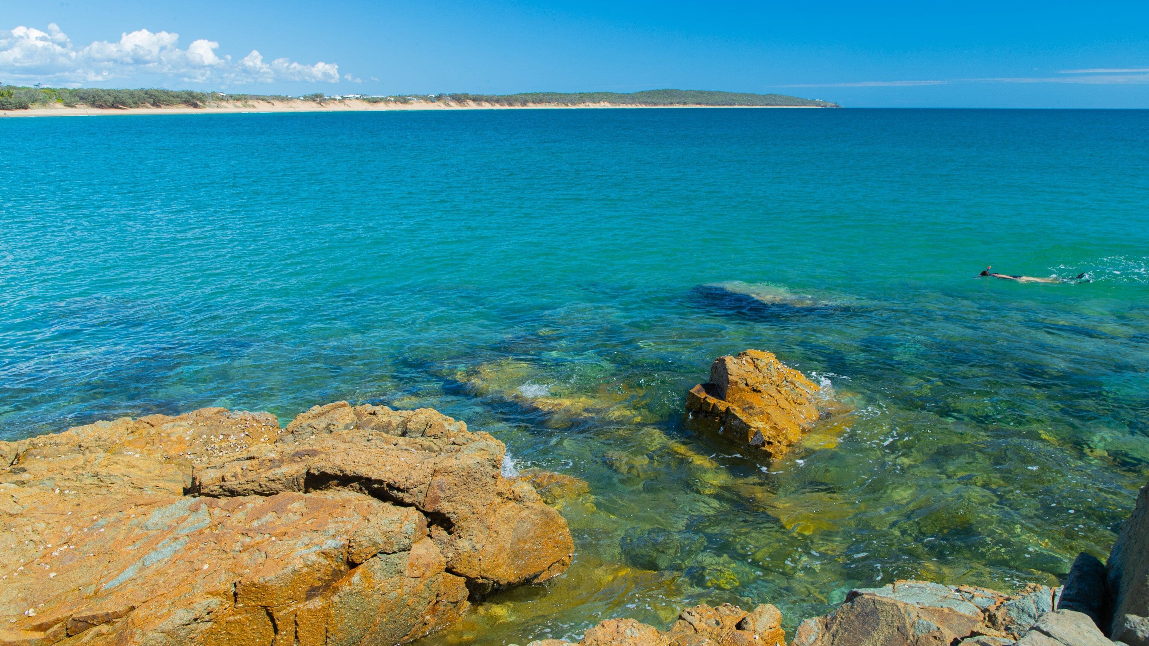 A coastal landscape with clear turquoise waters, rocky shorelines, and distant sandy beaches.