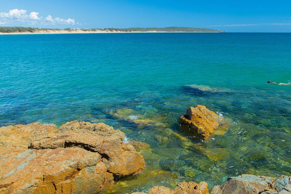 A coastal landscape with clear turquoise waters, rocky shorelines, and distant sandy beaches.