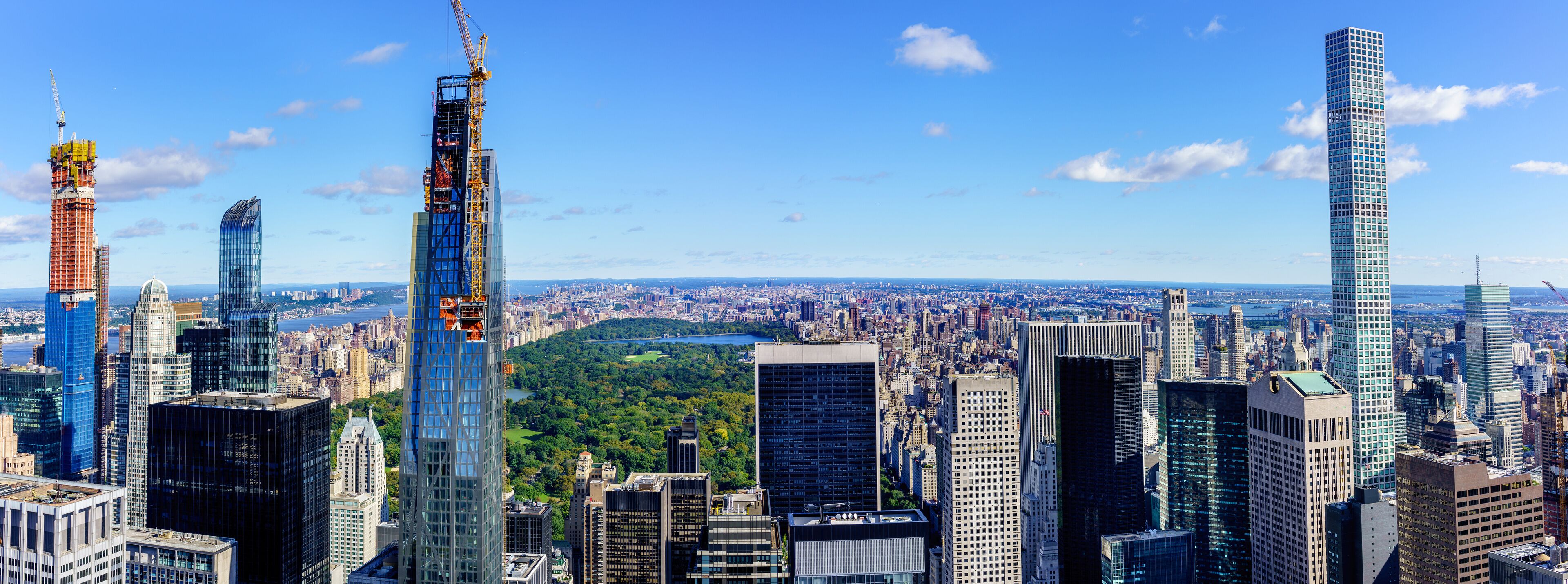 A cityscape with several high-rise buildings, including a construction crane, and a large park in the background.