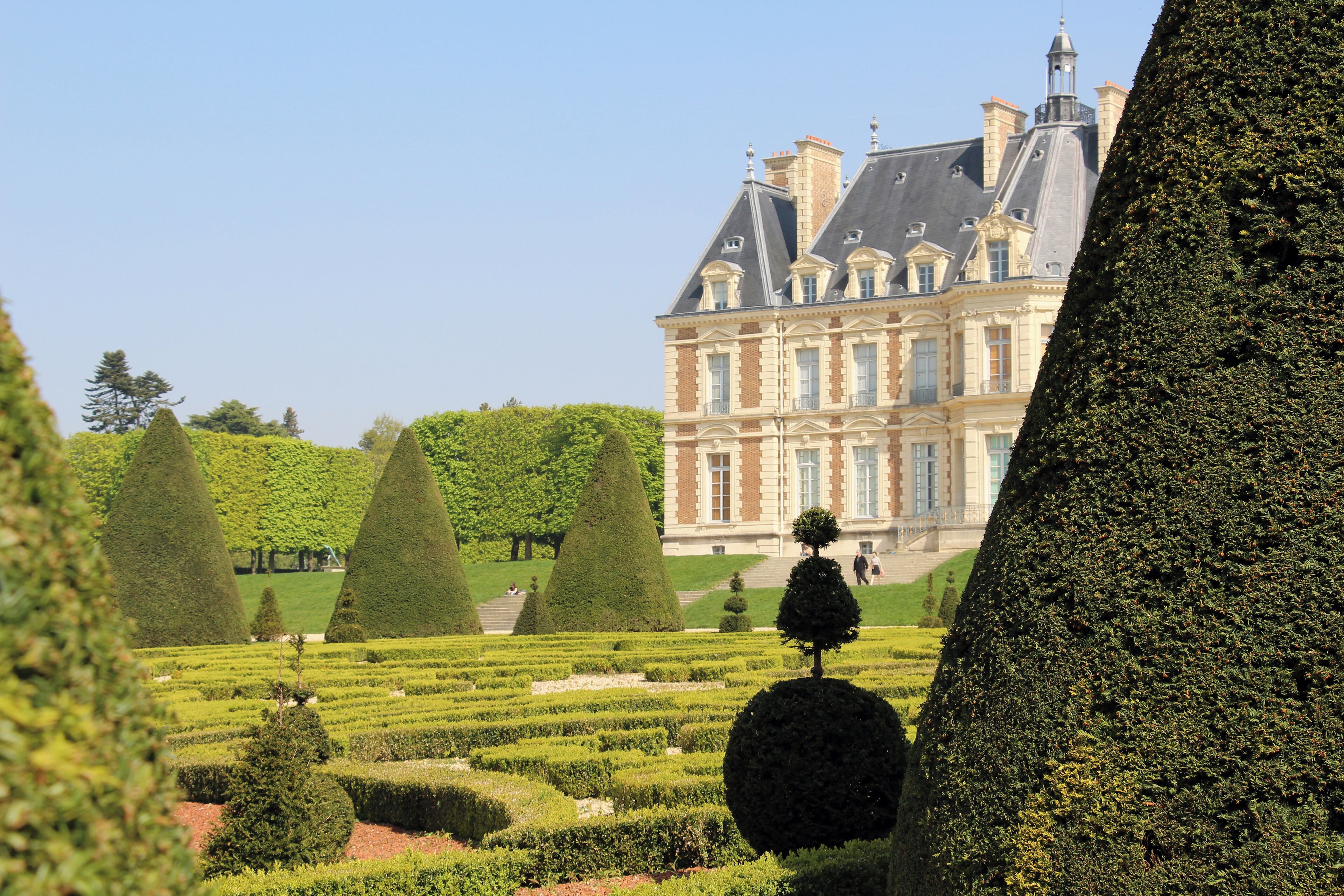 A grand château with manicured gardens, including topiary trees and neatly trimmed hedges.