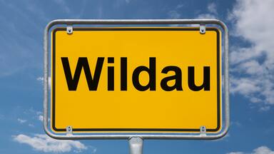 A yellow sign with the word "Wildau" against a blue sky with clouds.