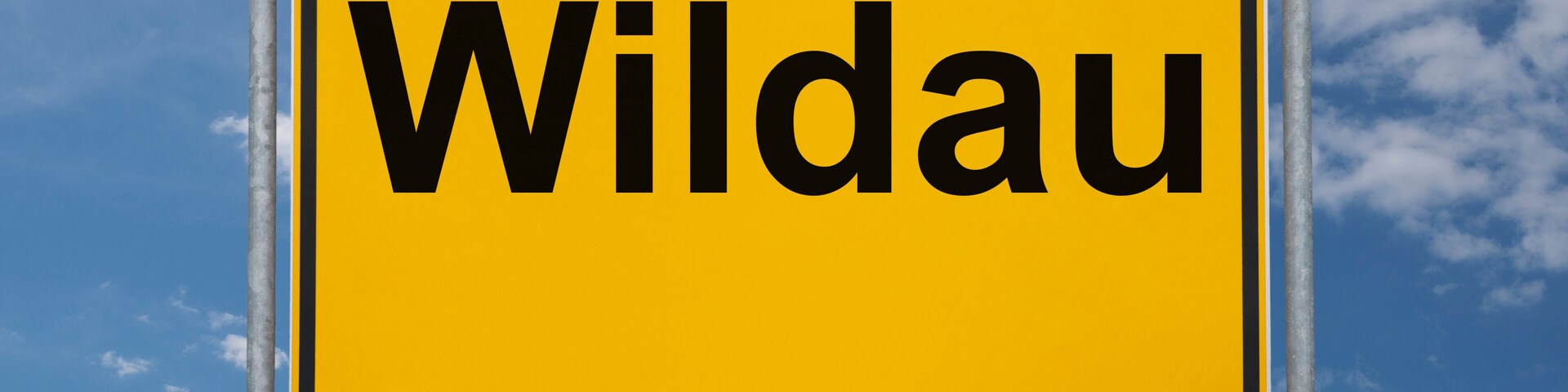 A yellow sign with the word "Wildau" against a blue sky with clouds.