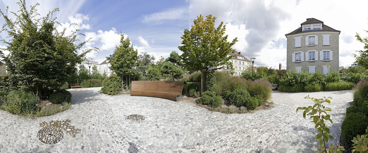 A landscaped garden with a stone pathway, wooden benches, and a variety of trees and shrubs.