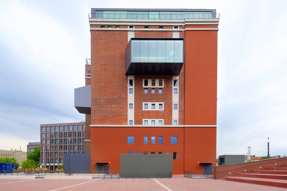 Un edifici modern amb façana de maó vermell, grans finestres i una estructura en voladís singular.