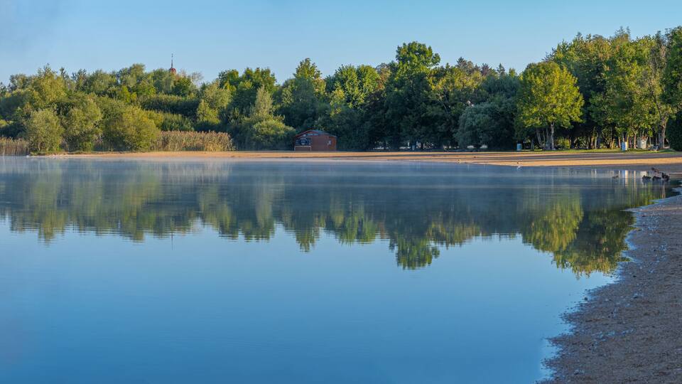 A calm lake with a wooden dock and a small building on the shore.