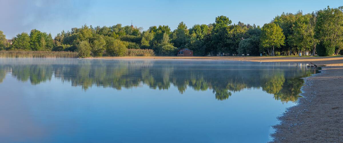 A calm lake with a wooden dock and a small building on the shore.