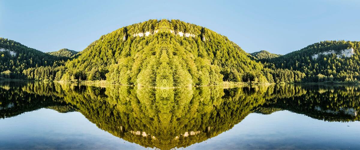 A calm lake with a forested island reflecting in the water.