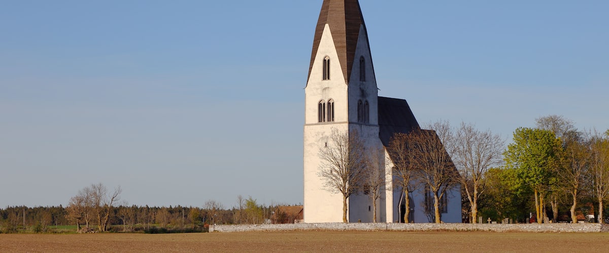 A church with a tall, pointed tower and a large open field in the foreground.