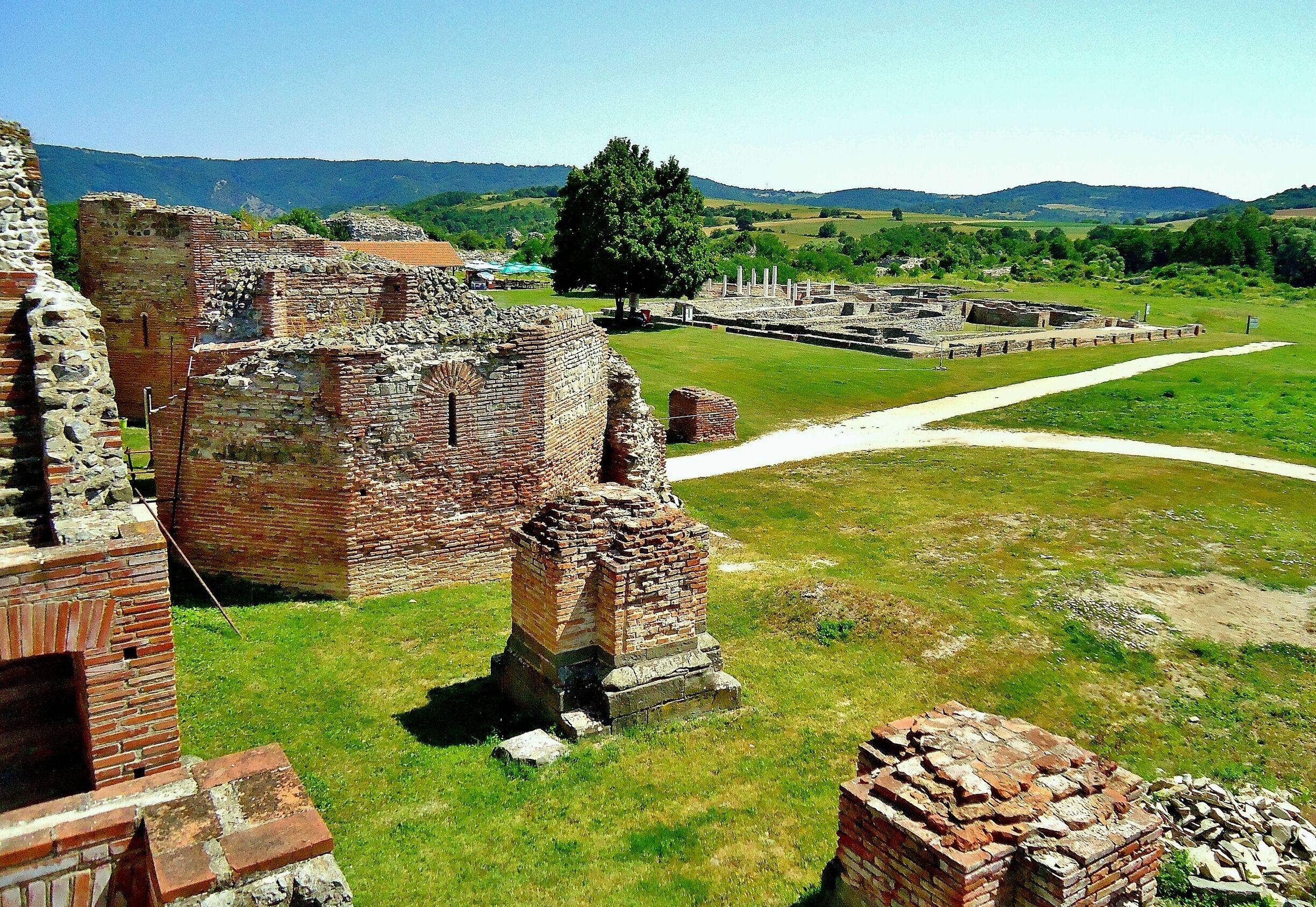 Ancient brick ruins with a grassy field and distant hills.
