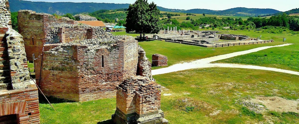 Ancient brick ruins with a grassy field and distant hills.